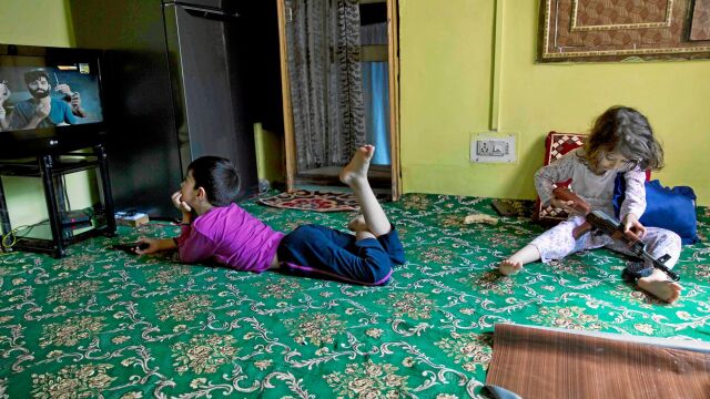 Un niño ve la televisión mientras su hermana juega con un arma de juguete en Srinagar