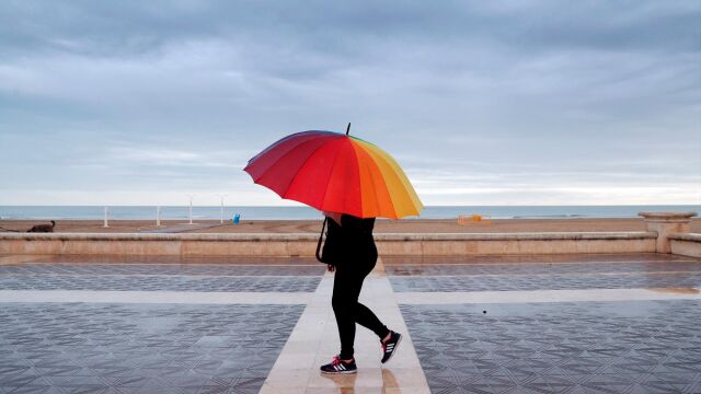 Una persona pasea por la playa de la Malvarrosa protegida con un paraguas
