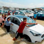 Varios vecinos de Orihuela empujan un coche para sacarlo de un parking totalmente inundado