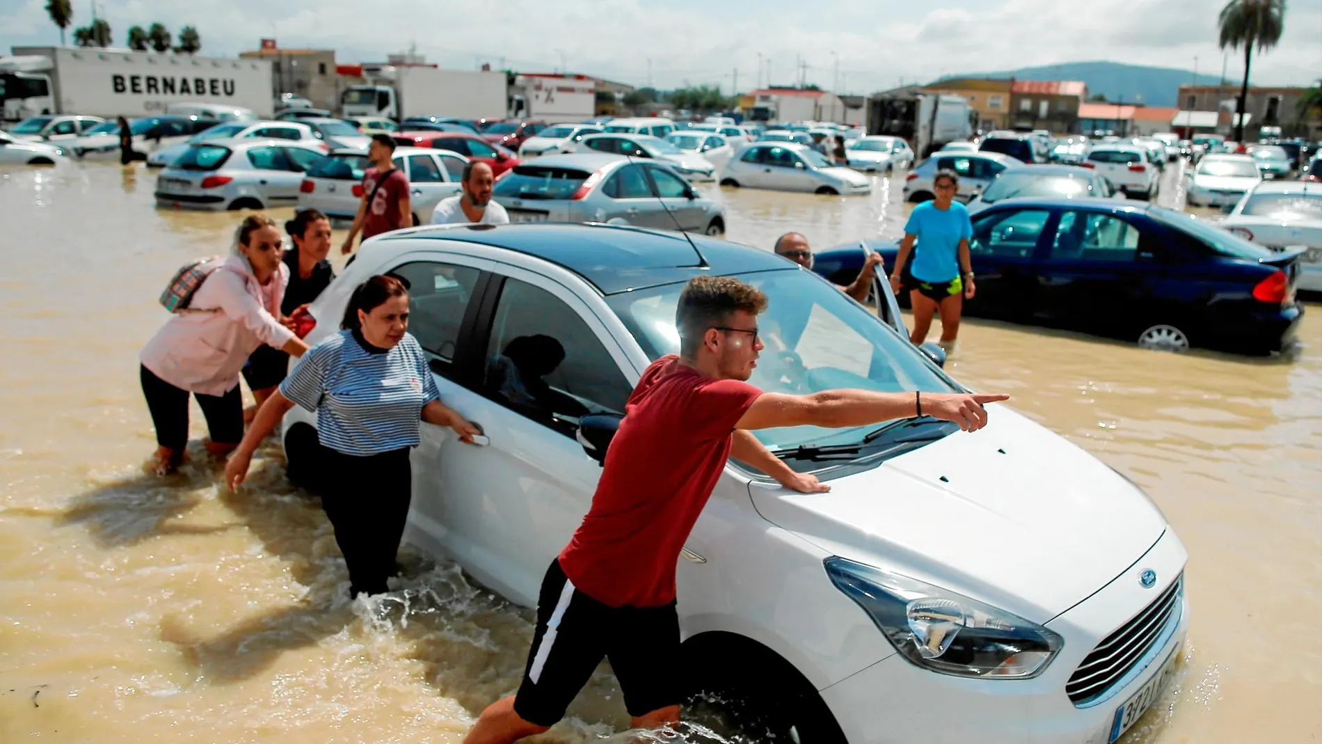 Varios vecinos de Orihuela empujan un coche para sacarlo de un parking totalmente inundado