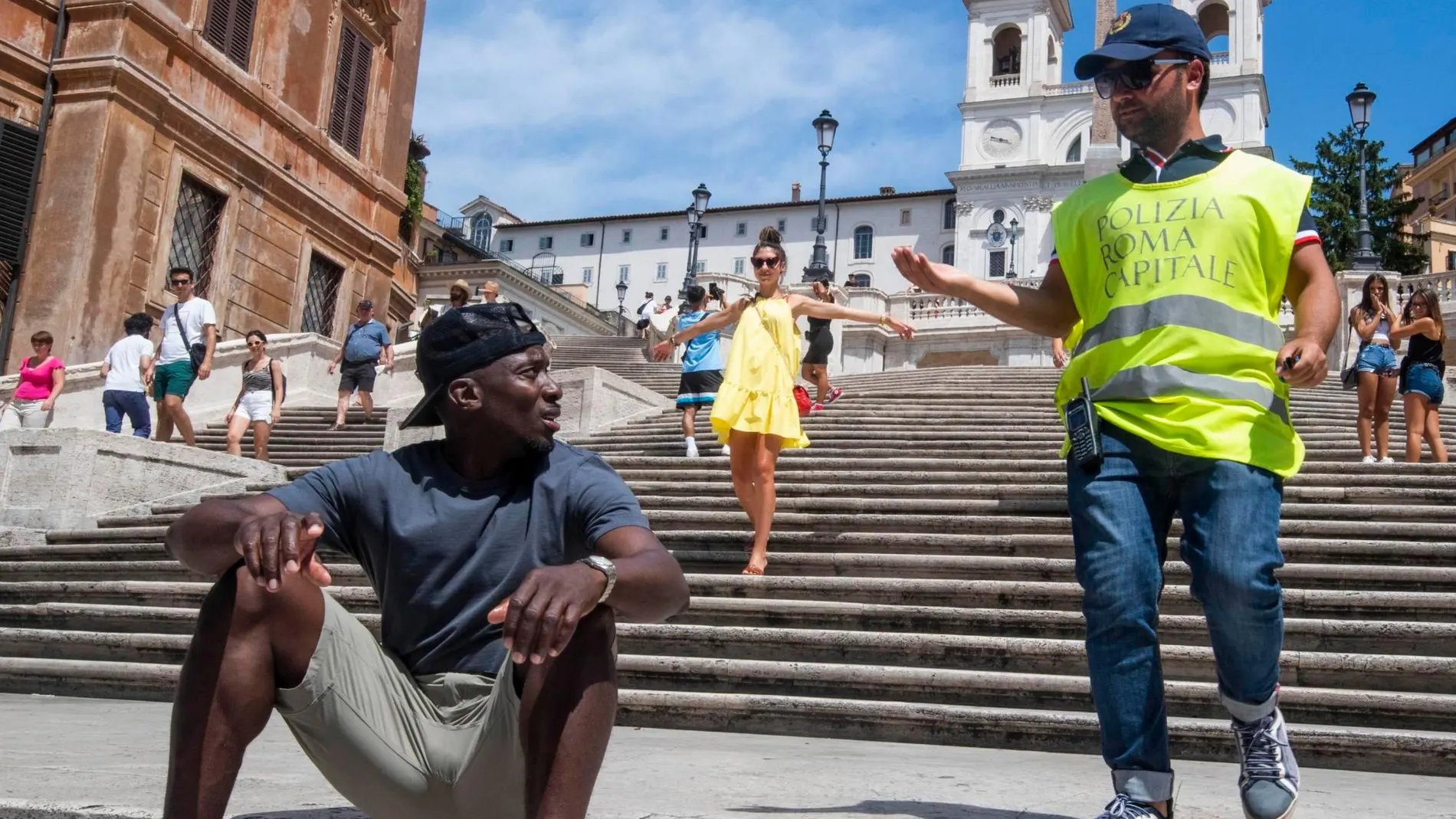 Un policía informa a un turista de la prohibición de sentarse en las escaleras de la Plaza de España/ EFE