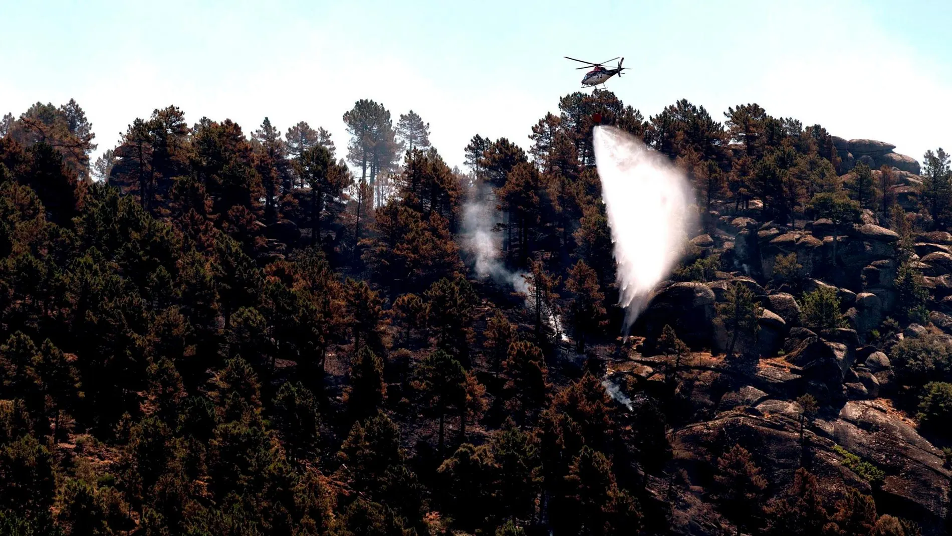 Un helicóptero echa agua sobre la zona afectada de El Arenal, en el Valle del Tiétar, que sigue activo aunque la situación ha mejorado
