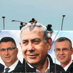 Operarios cuelgan un cartel electoral durante la campaña de marzo donde aparece Netanyahu y candidatos de su partido/Reuters