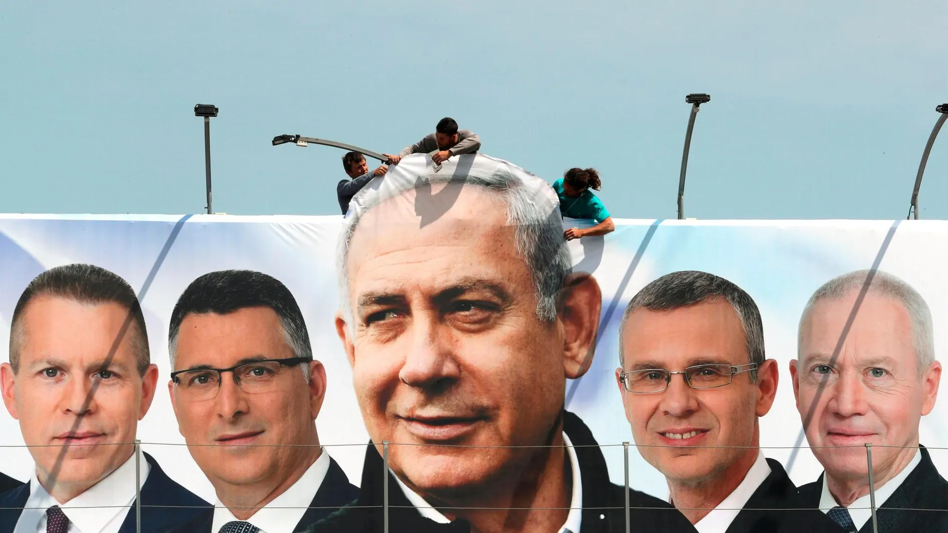 Operarios cuelgan un cartel electoral durante la campaña de marzo donde aparece Netanyahu y candidatos de su partido/Reuters