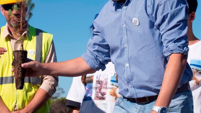 El presidente del Gobierno de Andalucía, Juanma Moreno, sujeta una planta que le ofrecieron los alumnos del IES Odón Betanzos Palacios de Mazagón (Huelva) para participar en una actividad de reforestación en la zona afectada por el incendio de 2017, dentro de los actos conmemorativos del 50 aniversario del Parque de Doñana esta semana / Foto: Efe
