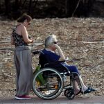 Una cuidadora ayuda a una persona dependiente a tomar el aire en un parque