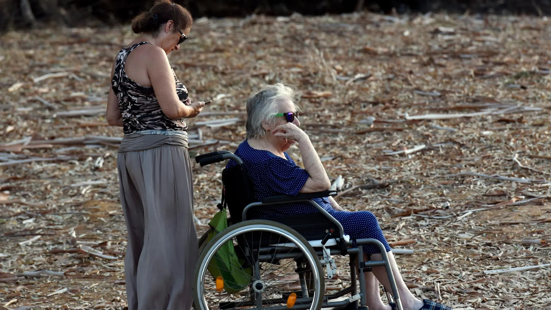 Una mujer ayuda a una persona dependiente a tomar el aire en un parque