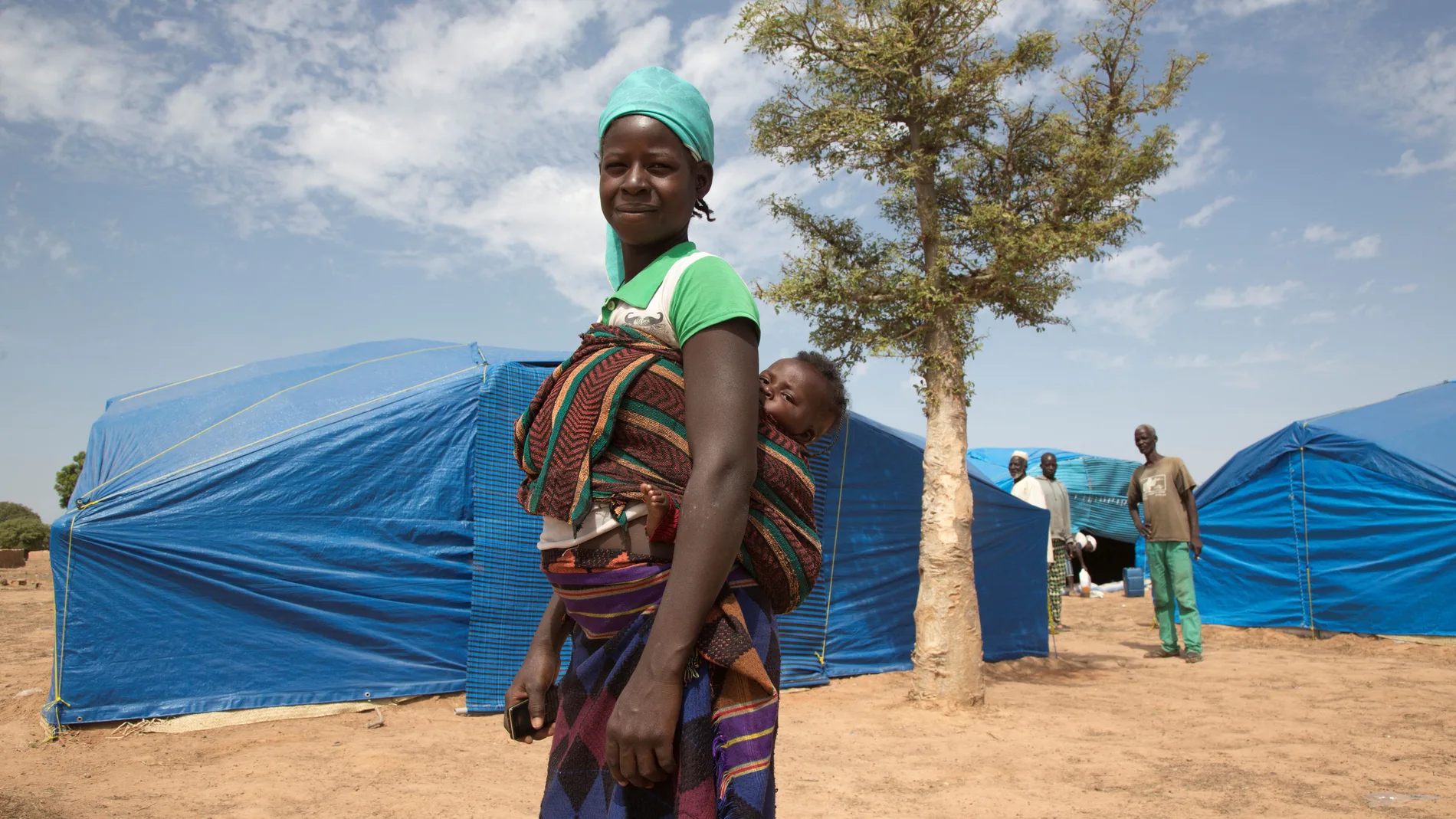 A woman carries her child as she stands at an IDP camp in Pissila