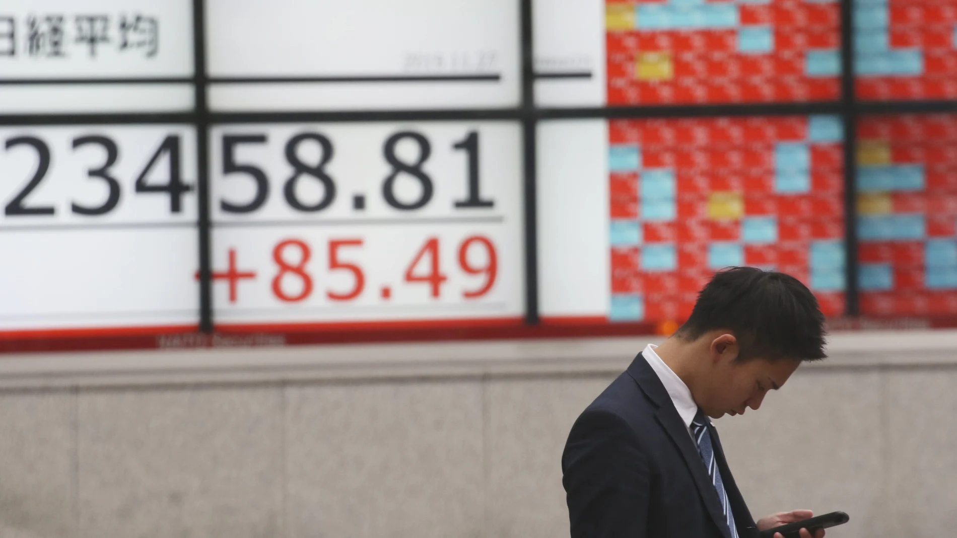 Un hombre mira su móvil junto a unos paneles con los indicadores de la bolsa en Tokio. (AP Photo/Koji Sasahara)
