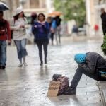 Un indigente pidiendo en la calle bajo la lluvia