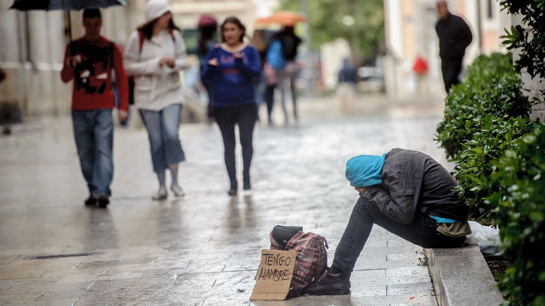 Un indigente pidiendo en la calle bajo la lluvia