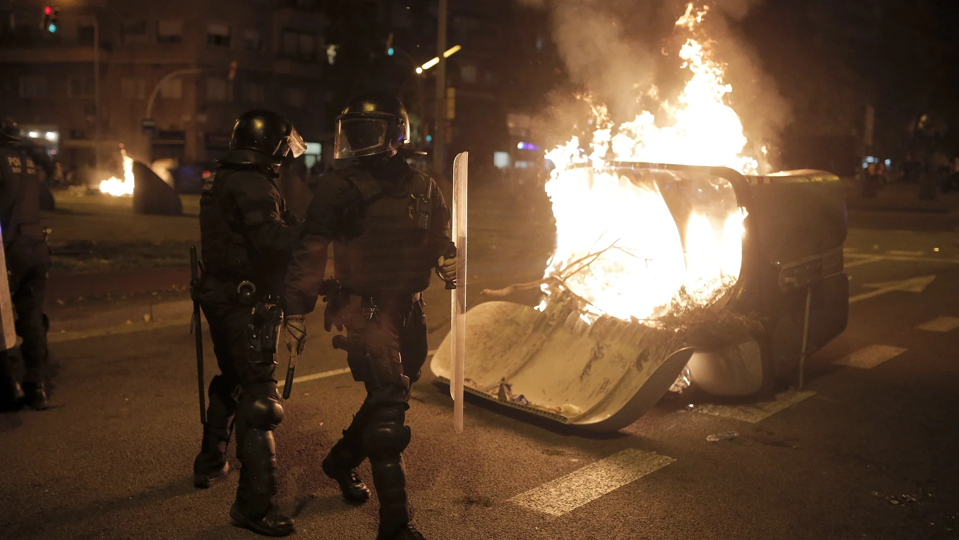 Police officers walk past a burning garbage container toward the end of a Catalan pro-independence protest outside the Camp Nou stadium in Barcelona, Spain, Wednesday, Dec. 18, 2019. Thousands of Catalan separatists protested around and inside Barcelona's Camp Nou Stadium during Wednesday's match against fierce rival Real Madrid. (AP Photo/Joan Mateu)