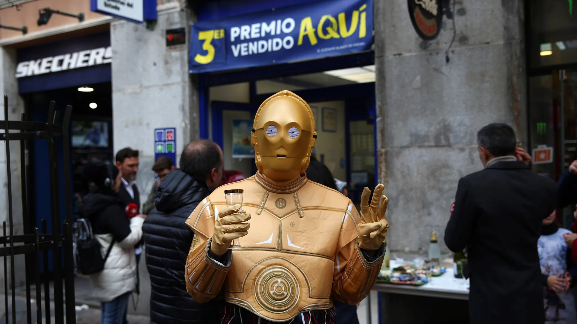 Una persona disfrazada del robot de la Guerra de las Galaxias C-3PO celebra en la administración de lotería 150 en la calle Arenal de Madrid donde se ha vendido una serie del tercer premio del Sorteo Extraordinario de Navidad, el número 00750.