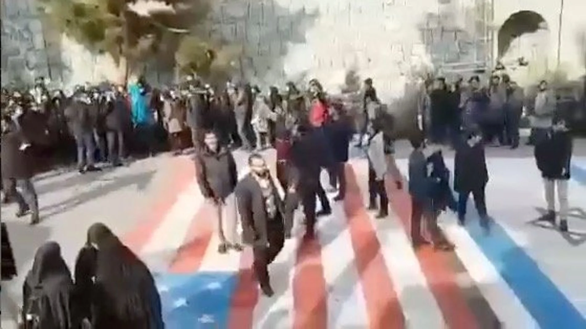 Social media video still shows several people walking on U.S. and Israeli flags while others avoid stepping on the flags by walking around them, at the Shahid Beheshti University in Tehran