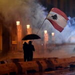 Dos manifestantes ondean la bandera de Líbano bajo el amparo de un paragüas en Beirut. EFE/EPA/WAEL HAMZEH