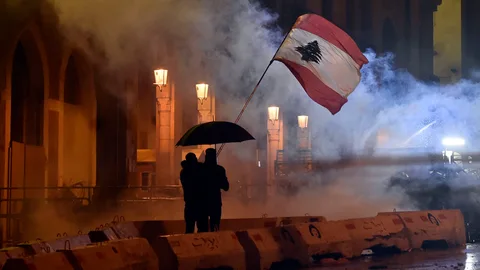 Dos manifestantes ondean la bandera de Líbano bajo el amparo de un paragüas en Beirut. EFE/EPA/WAEL HAMZEH