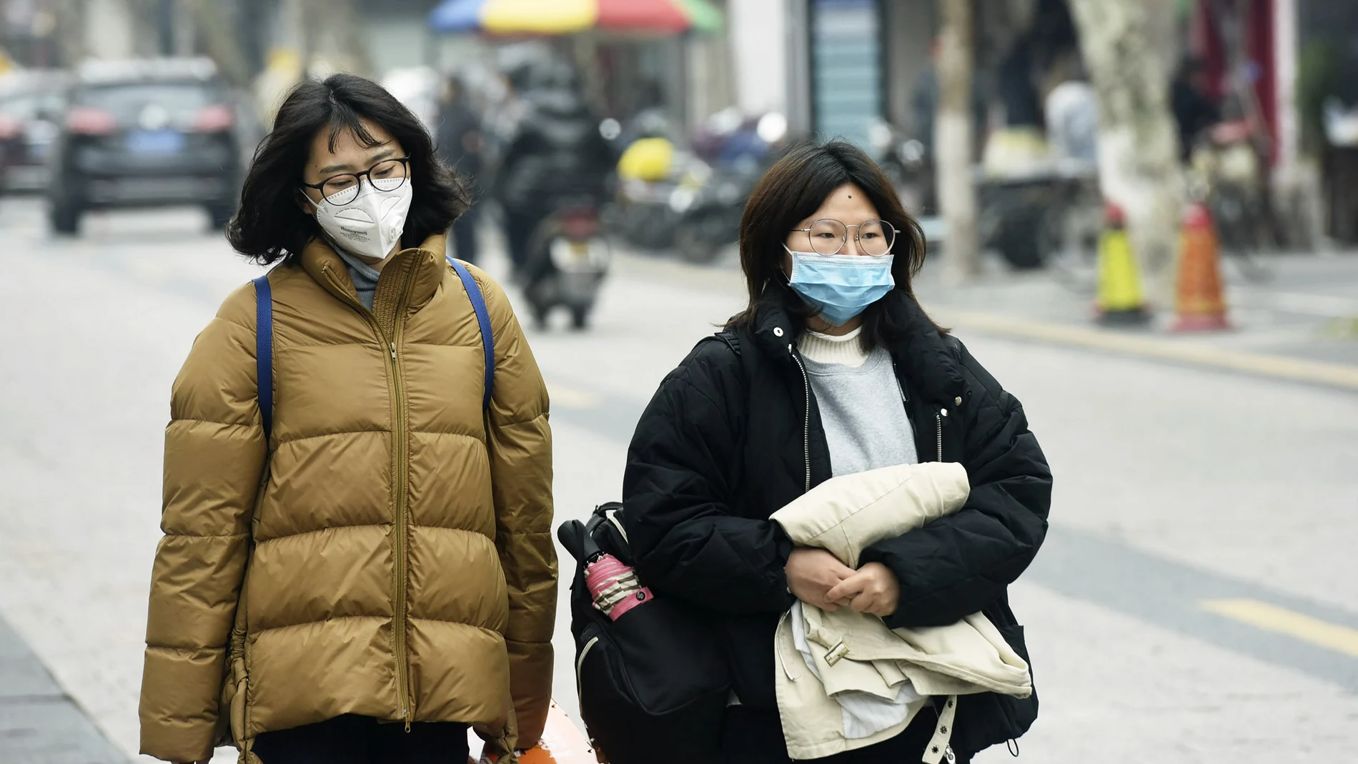 Women wear face masks as they walk down a street in Hangzhou in eastern China's Zhejiang province, Tuesday, Jan. 21, 2020. Face masks sold out and temperature checks at airports and train stations became the new norm as China strove Tuesday to control the outbreak of a new coronavirus that has reached four other countries and territories and threatens to spread further during the Lunar New Year travel rush. (Chinatopix via AP)