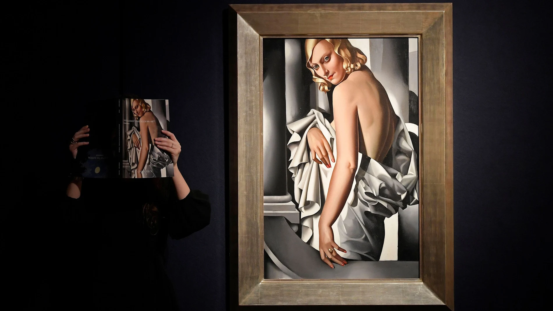 An employee poses as she views a sales catalogue next to 'Portrait de Marjorie Ferry' by Tamara de Lempecka ahead of Impressionist, Modernist and Surreal sales at Christie's auction house, London, Britain, January 30, 2020. REUTERS/Toby Melville NO RESALES. NO ARCHIVES.