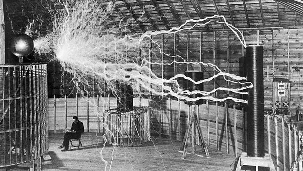 Nikola sentado al lado de una bobina de Tesla, en su laboratorio de Colorado Springs (1899)