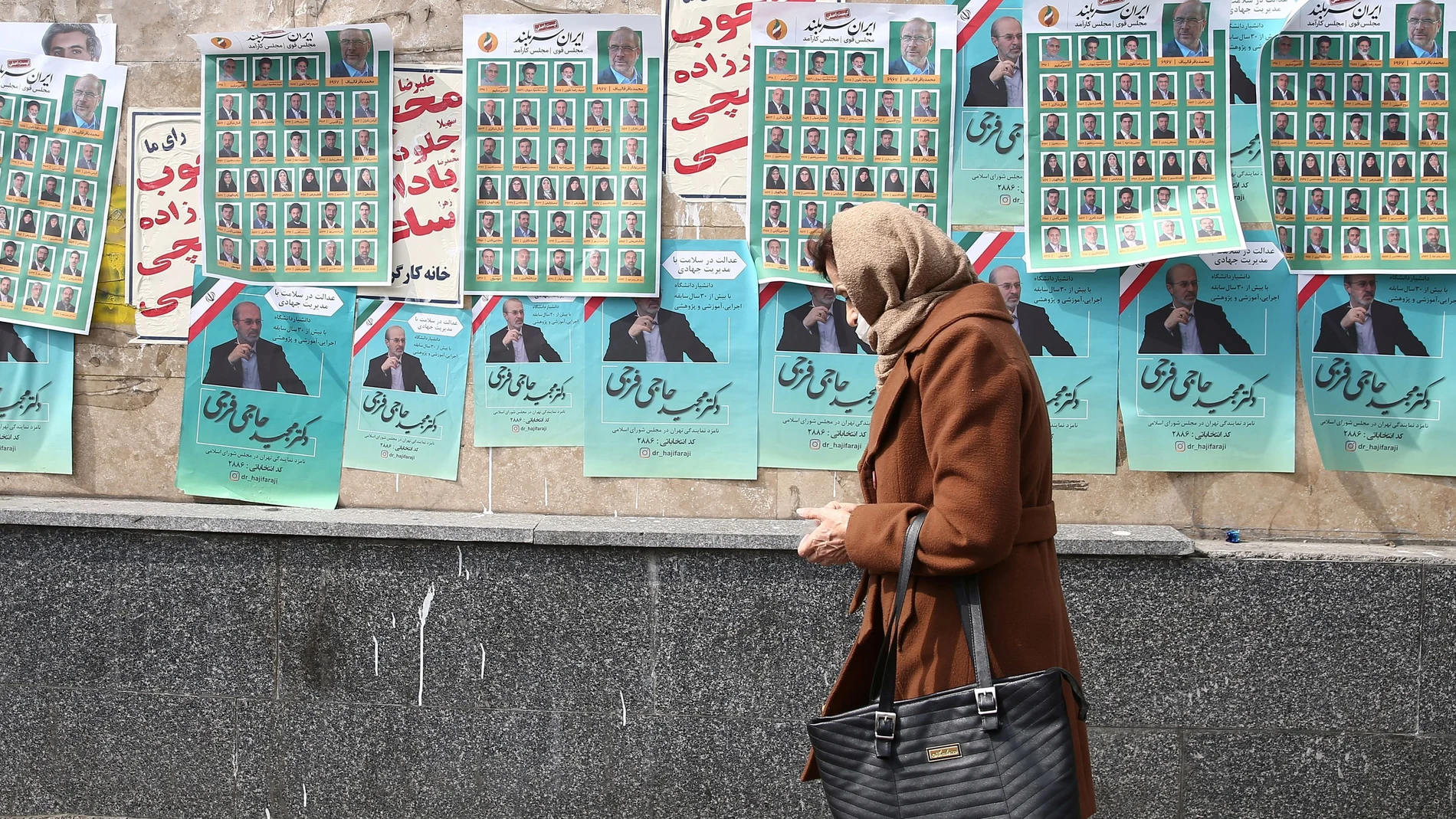 A woman walks past parliamentary election campaign posters in Tehran