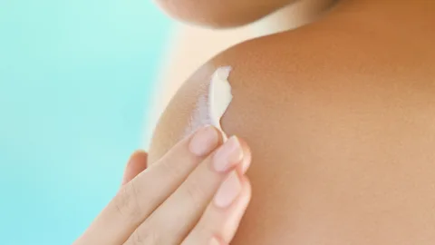 Extreme close up of a young woman applying lotion over her shoulder