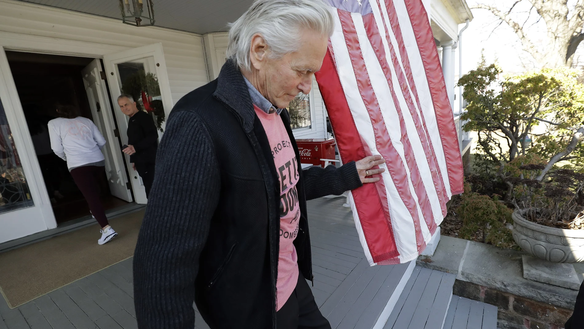 Actor Michael Douglas, front, steps off the front porch of Aileen Eleey, left, and her husband Peter Eleey's, second from left, home after canvasing for Democratic presidential candidate and former New York City Mayor Mike Bloomberg, not shown, Sunday, Feb. 23, 2020, in Quincy, Mass. (AP Photo/Steven Senne)