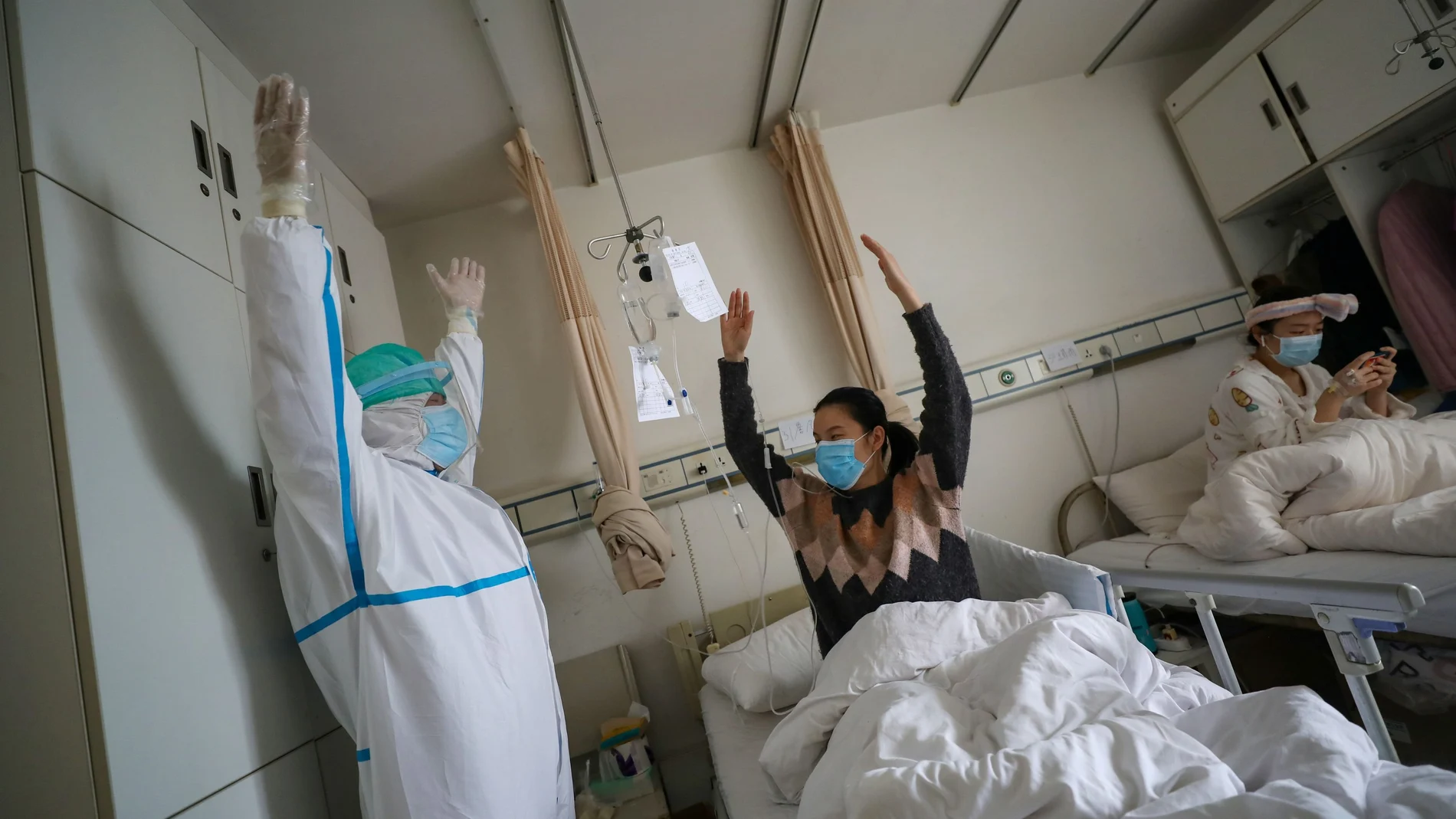 Medical worker in a protective suit shows a patient gestures of an exercise for rehabilitation at a ward of Wuhan Red Cross Hospital in Wuhan