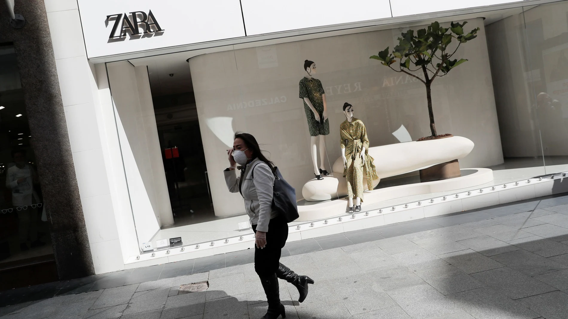 A woman wearing a protective mask and plastic gloves walks past a Zara store in Madrid