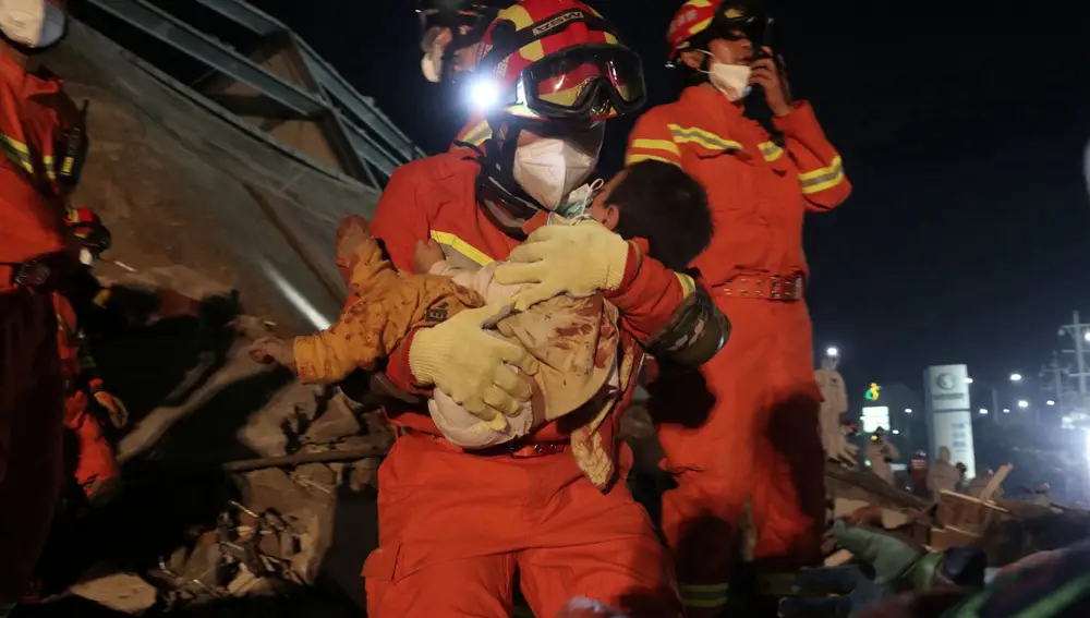 Servicios de emergencia rescatando a un niño de entre los escombros