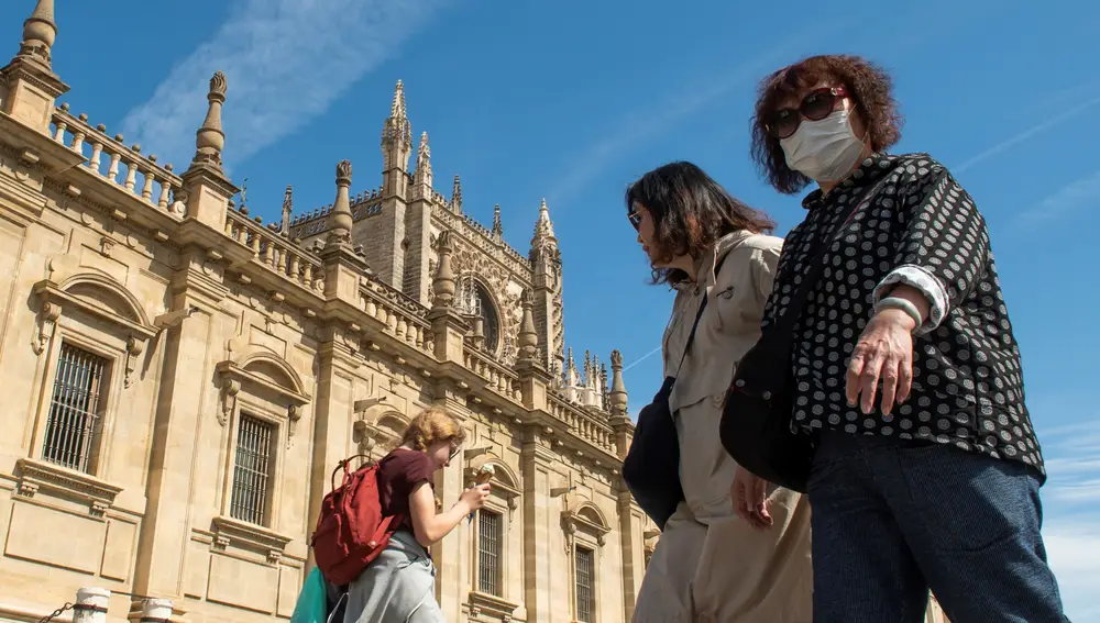Dos turistas, una de ellas con mascarilla, pasean junto a la Catedral de Sevilla.