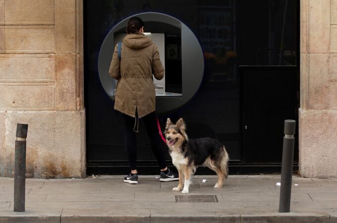 Una mujer saca dinero de un cajero y pasea a su perro en Barcelona