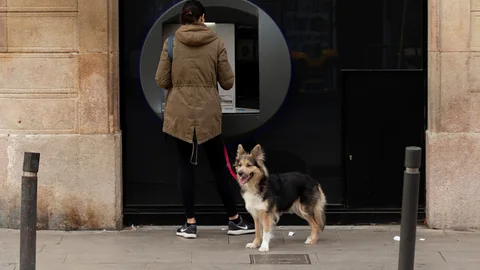 Una mujer saca dinero de un cajero y pasea a su perro en Barcelona