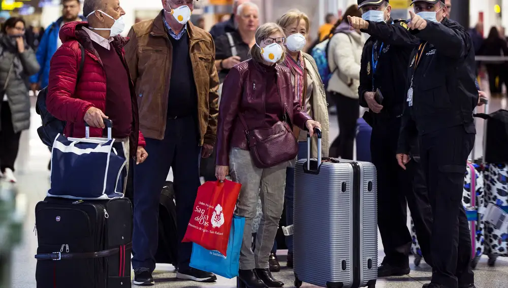 Un grupo de pasajeros atiende las indicaciones de agentes de la Policía Nacional en el Aeropuerto Internacional de Málaga, en la que está prevista la llegada hoy del II Batallón de Intervención en Emergencias (UME), dentro de las funciones de seguridad y tareas de desinfección por el coronavirus