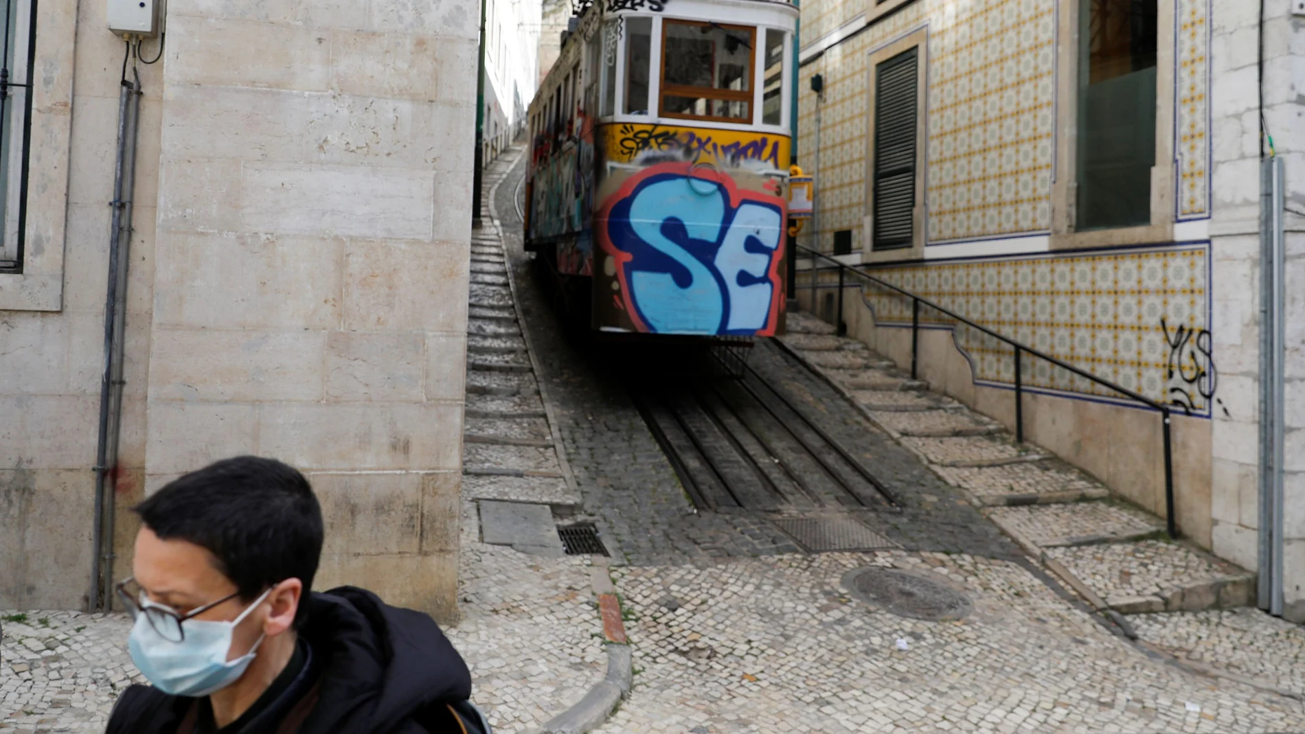 A woman is pictured wearing a mask as she walks next to a tram in downtown Lisbon