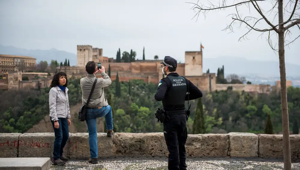 Un policía con mascarilla informa a dos turistas en el Mirador de San Nicolás, frente a la Alhambra