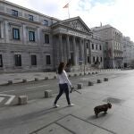 -FOTODELDIA- MADRID, 16/03/2020.- Una mujer pasea con su perro ante el Congreso de los Diputados, en Madrid. La capital, al igual que el resto de España, vive este lunes su primer día laboral de aplicación del decreto de alarma, que supone entre otras medidas la restricción de la movilidad, lo que disminuirá de nuevo notablemente el tráfico. EFE/Kiko Huesca