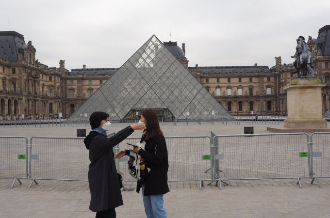 Turistas con máscaras faciales se paran frente al Museo del Louvre cerrado, en medio del brote de coronavirus.