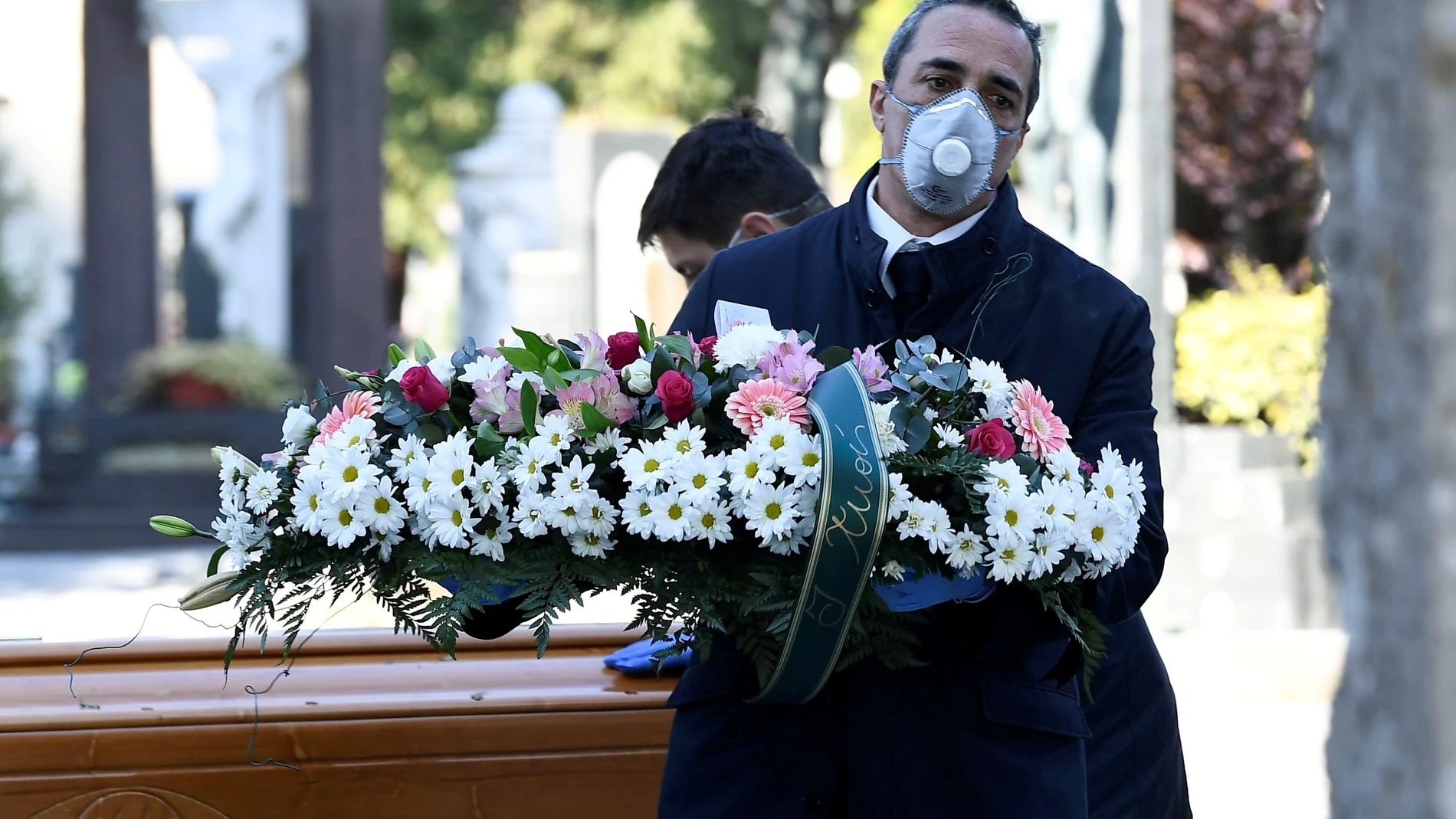 FILE PHOTO: Cemetery workers and funeral agency workers in protective masks transport a coffin of a person who died from coronavirus disease (COVID-19), into a cemetery in Bergamo