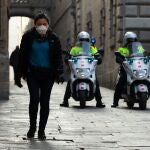 Una persona camina por una calle del centro histórico de Barcelona junto a una patrulla de los Mossos d'Esquadra