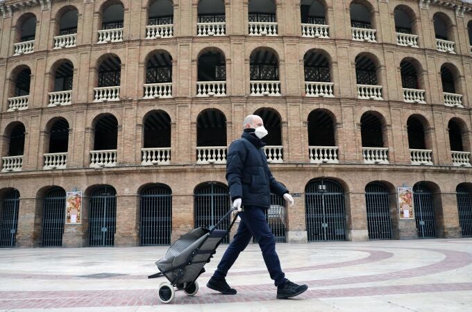 Una persona protejida con mascarilla y guantes pasa ante la plaza de Toros e valencia, hoy, sexto día desde que entró en vigor el Decreto de estado de alama.