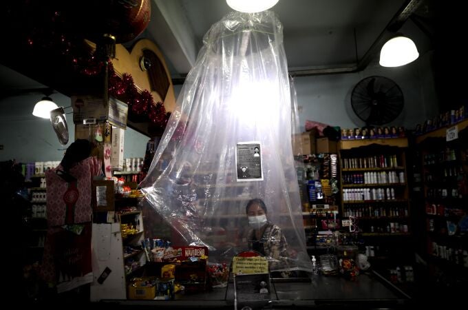 Una cajera del supermercado atiende a los clientes protegida por unas cortinas de plástico por coronavirus en Buenos Aires