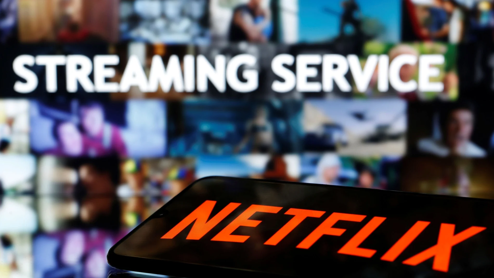 A smartphone with the Netflix logo lies in front of displayed "Streaming service" words in this illustration
