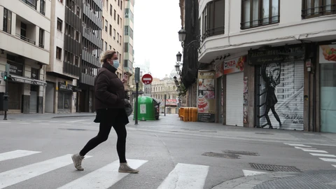 Una mujer protegida con una mascarilla camina por una calle vacía de Valencia