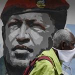 Un hombre cubierto con una mascarilla pasa delante de un grafiti del fallecido Hugo Chávez/AP