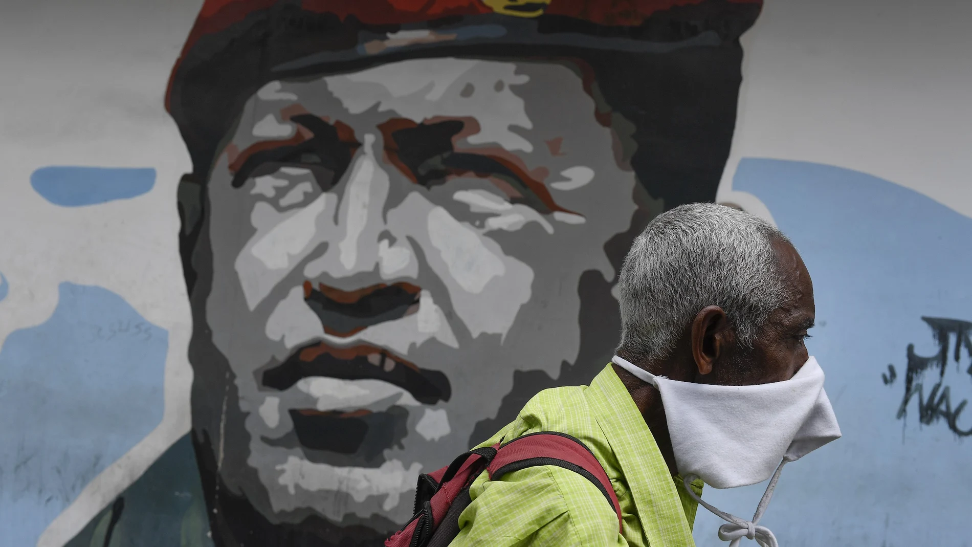 Un hombre cubierto con una mascarilla pasa delante de un grafiti del fallecido Hugo Chávez/AP