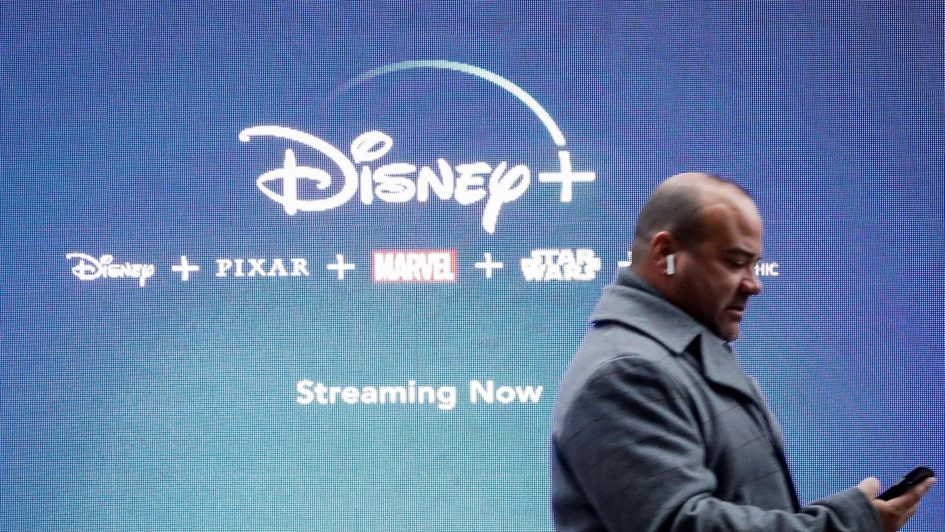 FILE PHOTO: A man looks at his phone as he passes by a screen advertising Walt Disney's streaming service Disney+ in New York, USA