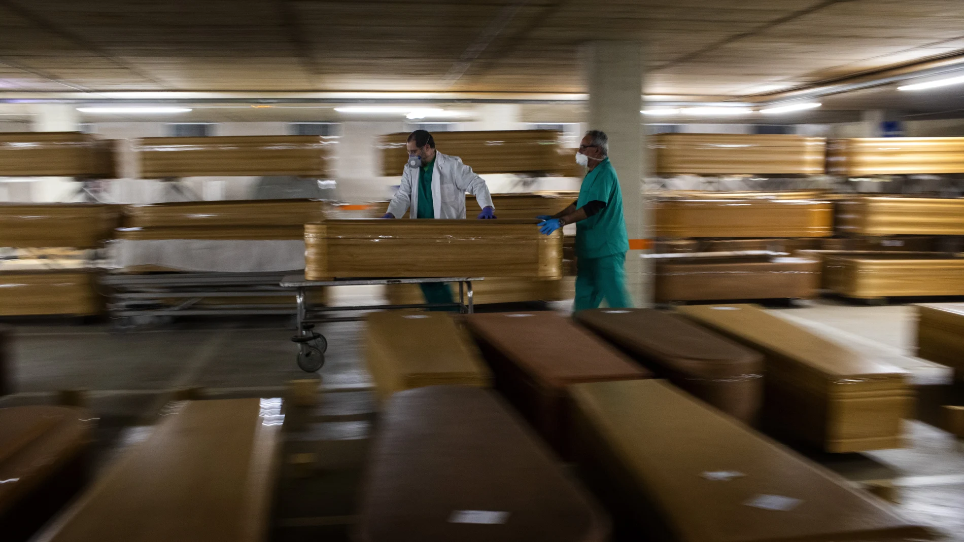 Workers move a coffin with the body of a victim of coronavirus as others coffins are stored waiting burial or cremation at the Collserola morgue in Barcelona, Spain, Thursday, April 2, 2020. The new coronavirus causes mild or moderate symptoms for most people, but for some, especially older adults and people with existing health problems, it can cause more severe illness or death. (AP Photo/Emilio Morenatti)