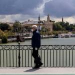 Un hombre pasea por el Puente de Triana de Sevilla con una mascarilla y guantes