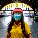 Una mujer se protege con una mascarilla y una pantalla en una estación en Bangkok, Tailandia