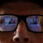 Una pantalla de televisión se refleja en las gafas de un anciano mientras contempla a Pedro Sánchez en una rueda de prensa